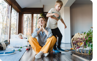 Trött mamma på golvet och lekande barn i bakgrunden