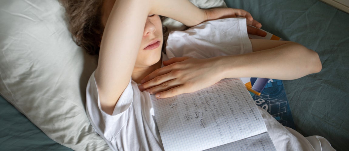 Uppgiven flicka med läxor liggandes i sängen.